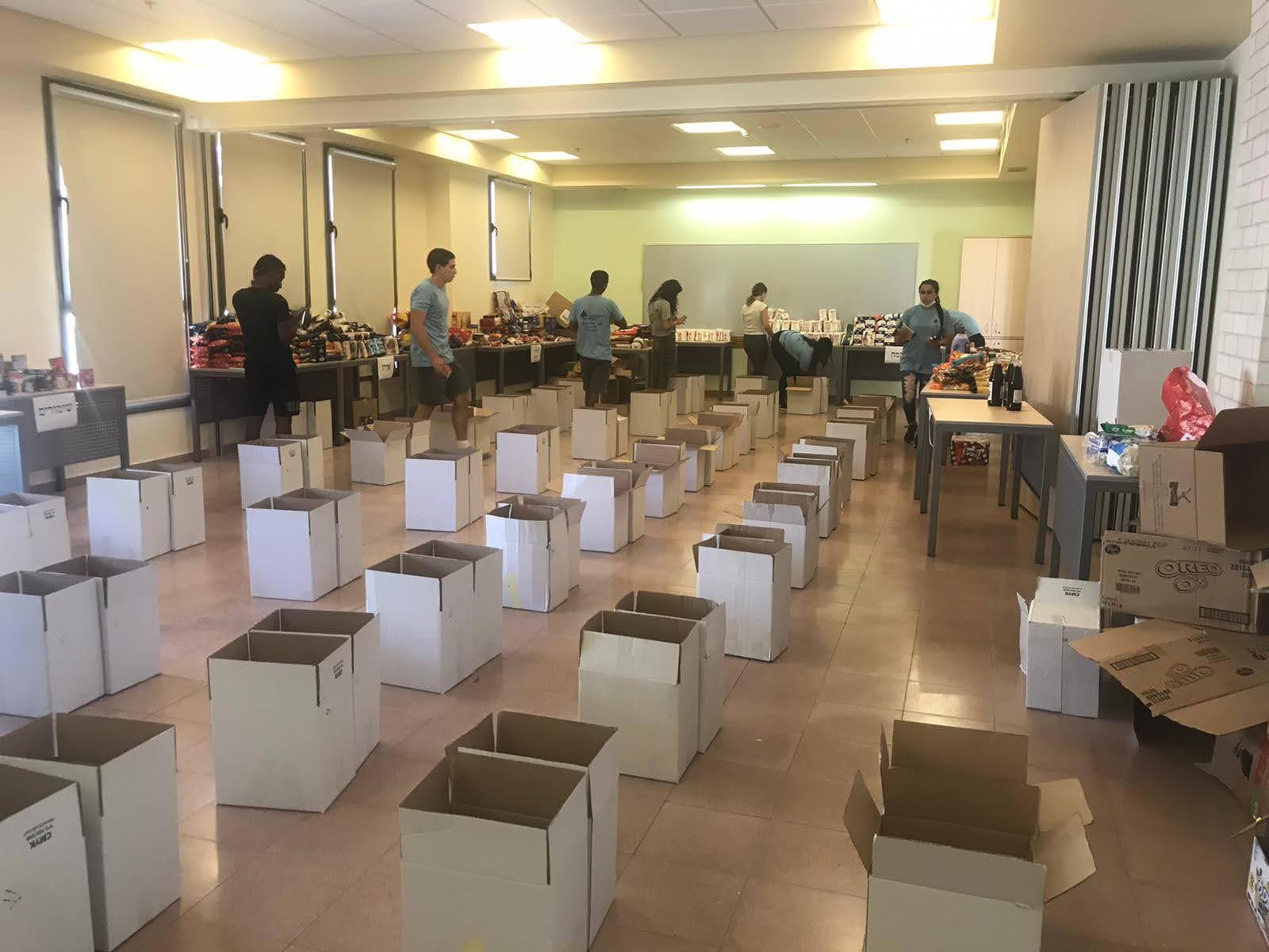 אולם גדול ובו עשרות קרטונים פתוחים בשורות, לקראת אריזת סלי מזון
