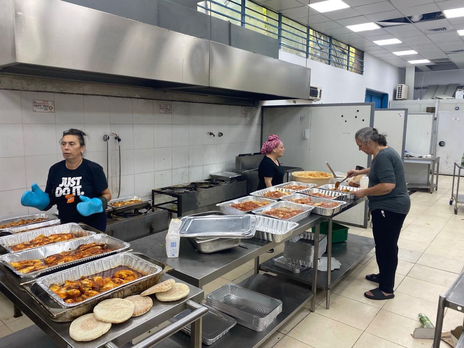 שלוש מתנדבות של העמותה עובדות במטבח תעשייתי בין עשרות תבניות אוכל חם