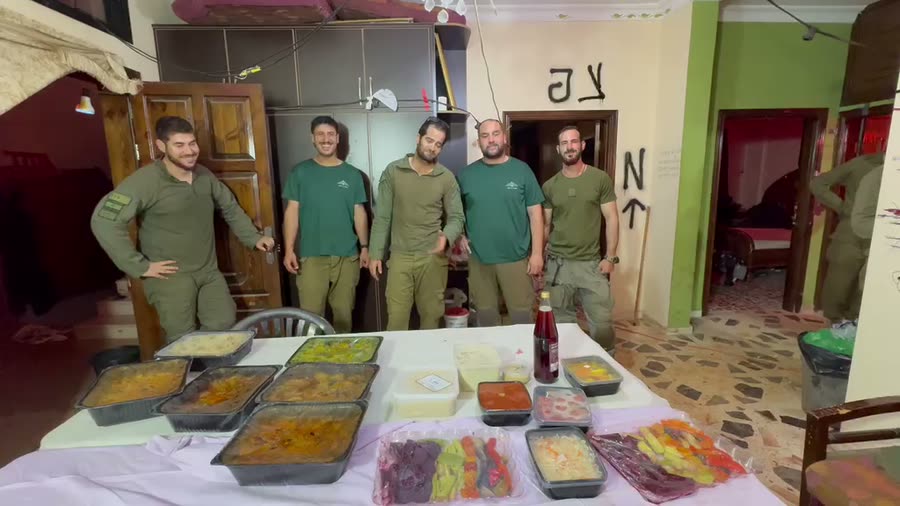 לוחמים עומדים סביב שולחן ערוך בתבניות אוכל חם שהגיעו מהעמותה
