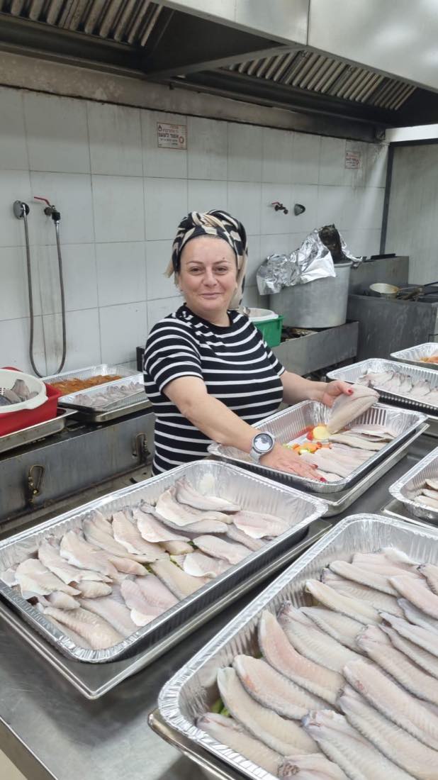 מתנדבת מכינה מגשי דגים במטבח העמותה לקראת ארוחות שבת