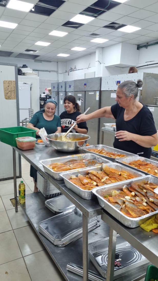 מתנדבות העמותה מכינות ומחלקות מנות חמות מתוך תבניות במטבח